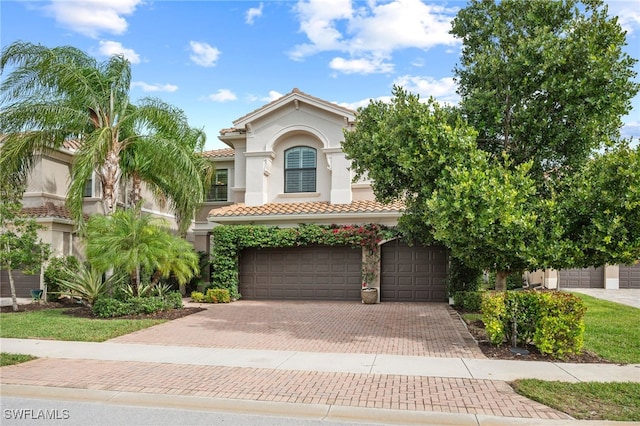 mediterranean / spanish-style home featuring decorative driveway, a tile roof, an attached garage, and stucco siding