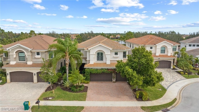 mediterranean / spanish-style house with a garage, a tiled roof, decorative driveway, a residential view, and stucco siding