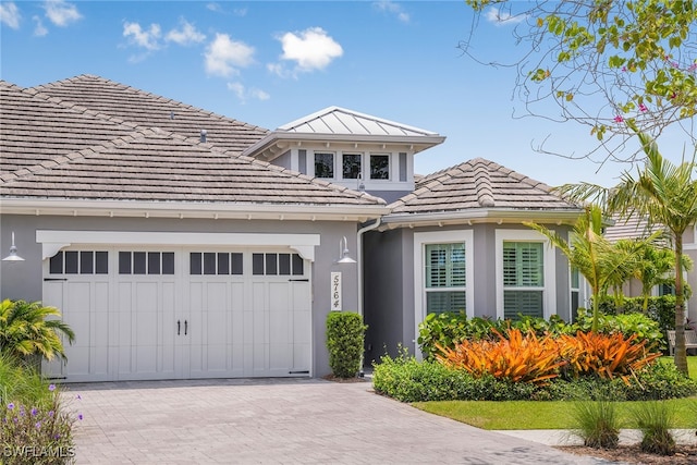 view of front of home featuring decorative driveway, a tile roof, an attached garage, and stucco siding