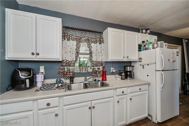 kitchen featuring light countertops, freestanding refrigerator, white cabinetry, and a sink