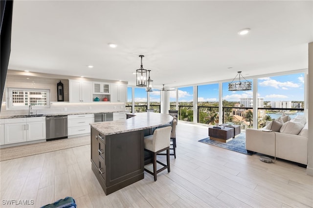 kitchen featuring light stone counters, white cabinets, a sink, a wall of windows, and dishwasher