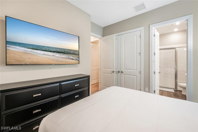 bedroom featuring a closet, visible vents, ensuite bath, and wood finished floors