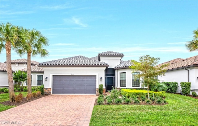 mediterranean / spanish-style home featuring a garage, stone siding, stucco siding, decorative driveway, and a front yard