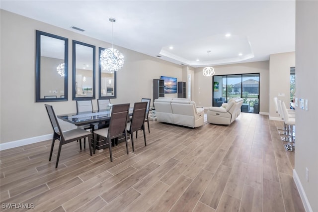 dining area with wood tiled floor, a raised ceiling, visible vents, and an inviting chandelier