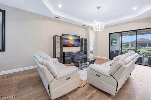 living room with a raised ceiling, visible vents, an inviting chandelier, ornamental molding, and wood tiled floor