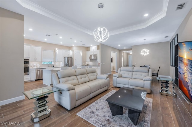 living area featuring a chandelier, a tray ceiling, wood finish floors, and baseboards