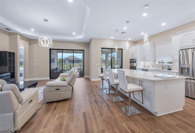 kitchen with a raised ceiling, light countertops, appliances with stainless steel finishes, open floor plan, and white cabinets