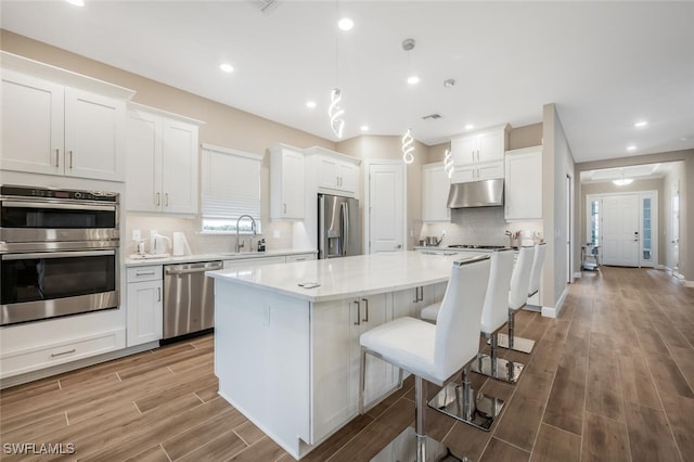 kitchen with under cabinet range hood, wood finish floors, a sink, appliances with stainless steel finishes, and a center island