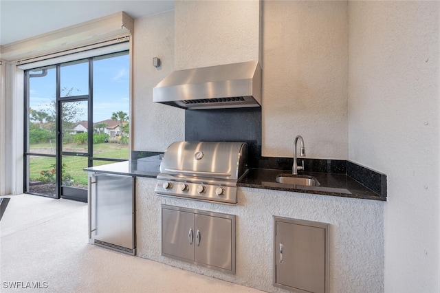 kitchen with a textured wall, dark stone countertops, fridge, wall chimney range hood, and a sink