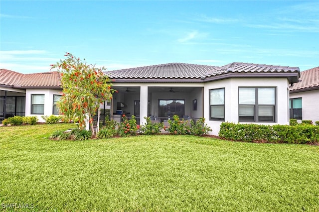 rear view of house with a sunroom, a tile roof, a lawn, and stucco siding