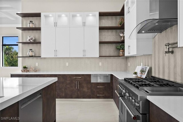 kitchen with open shelves, stainless steel appliances, light countertops, dark brown cabinetry, and wall chimney exhaust hood