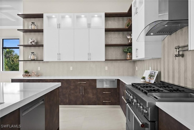 kitchen with open shelves, dark brown cabinetry, stainless steel stove, white cabinets, and wall chimney range hood