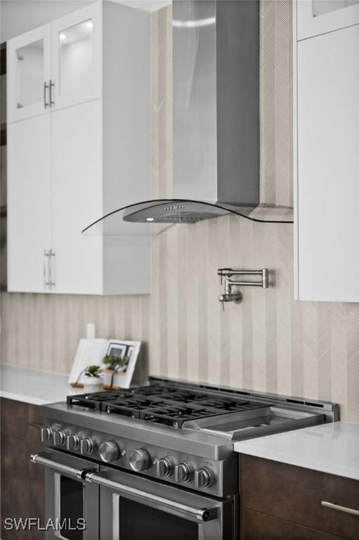 kitchen with double oven range, dark brown cabinetry, wall chimney exhaust hood, white cabinets, and light countertops