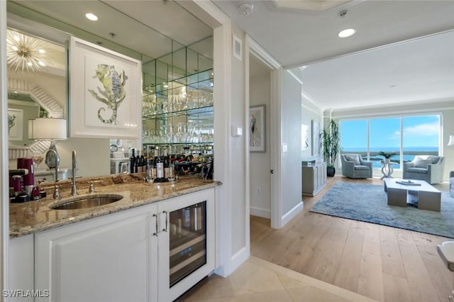 bar with light wood-style flooring, beverage cooler, a sink, ornamental molding, and indoor wet bar