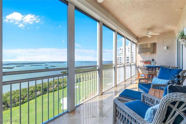 sunroom with a ceiling fan and a water view