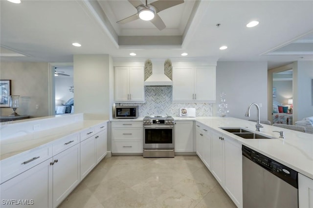 kitchen featuring custom range hood, a peninsula, a tray ceiling, stainless steel appliances, and a sink