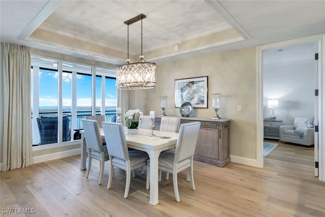 dining area featuring a raised ceiling, light wood-style flooring, and baseboards