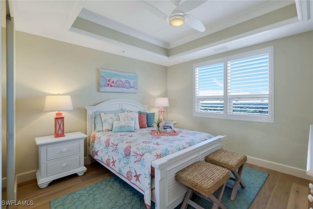 bedroom featuring a ceiling fan, a raised ceiling, baseboards, and wood finished floors