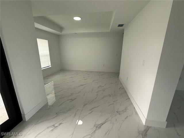 empty room featuring marble finish floor, a tray ceiling, visible vents, and baseboards