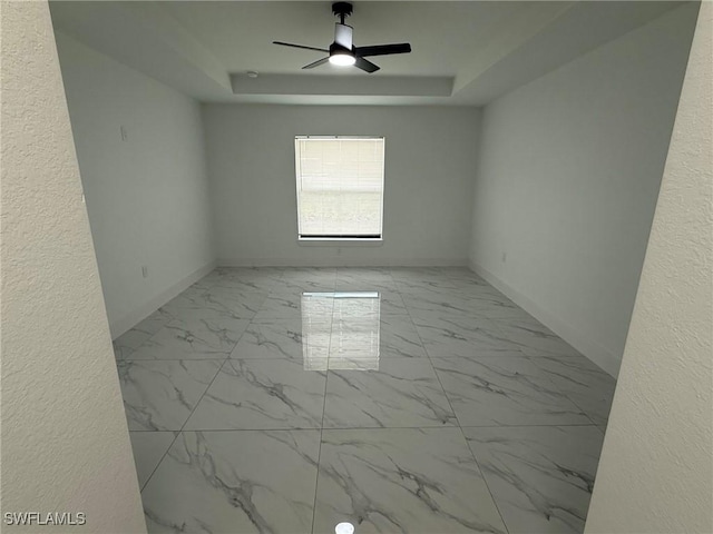 spare room with marble finish floor, baseboards, a raised ceiling, and a ceiling fan