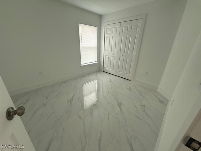 unfurnished bedroom with marble finish floor, baseboards, and a closet