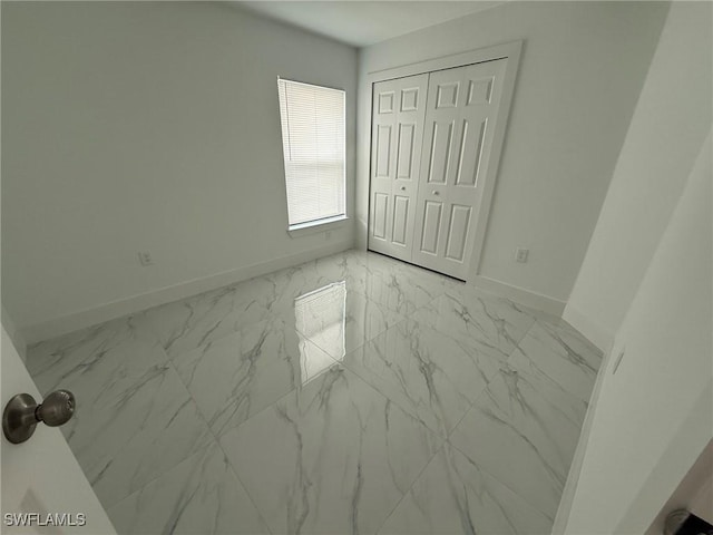 unfurnished bedroom featuring marble finish floor, a closet, and baseboards