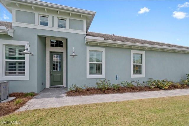 doorway to property with a lawn and stucco siding