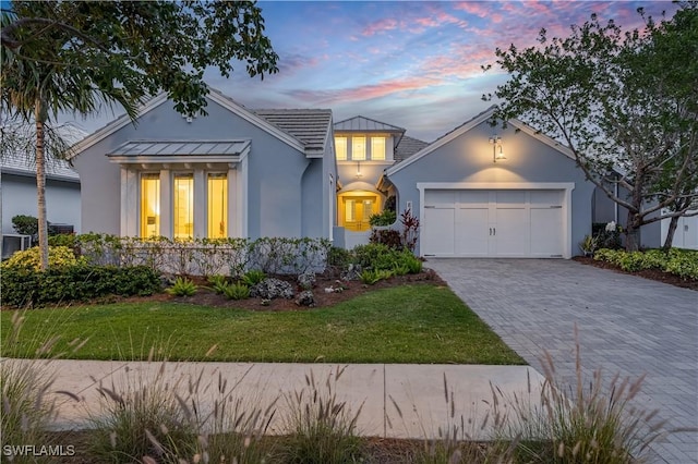 view of front facade with a garage, a yard, decorative driveway, and stucco siding