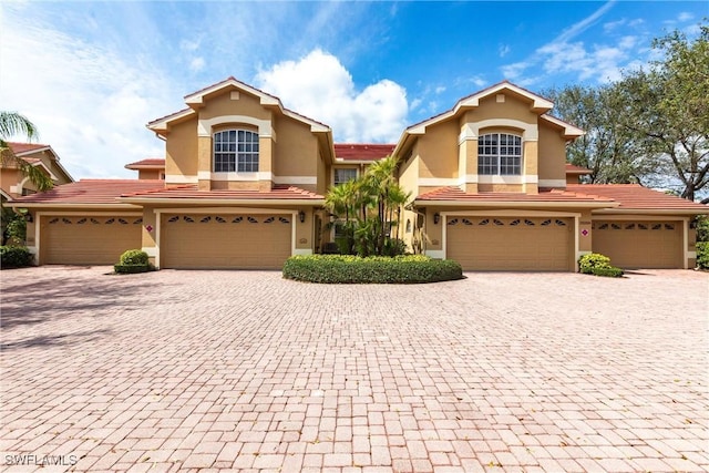 mediterranean / spanish-style home with a garage, a tiled roof, decorative driveway, and stucco siding