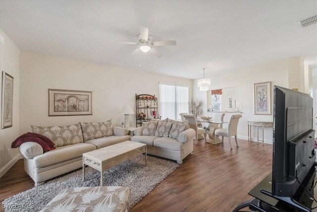 living area featuring baseboards, visible vents, wood finished floors, and ceiling fan with notable chandelier