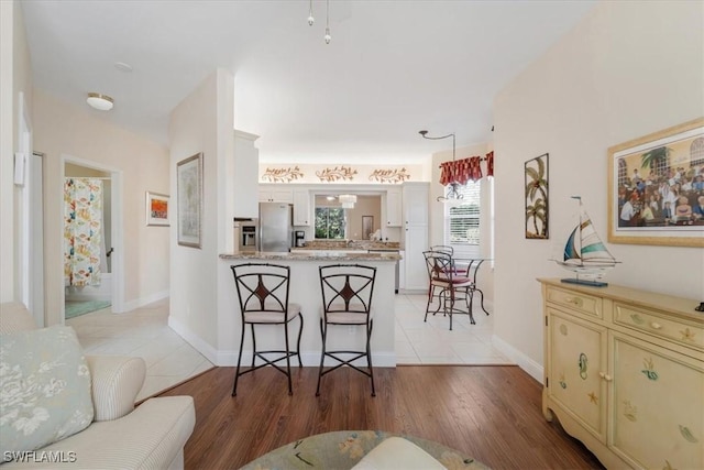 kitchen with light countertops, cream cabinets, freestanding refrigerator, a peninsula, and a kitchen breakfast bar