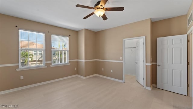 unfurnished bedroom with a closet, light wood-style flooring, a spacious closet, ceiling fan, and baseboards