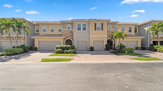 townhome / multi-family property with a garage, stone siding, decorative driveway, and stucco siding