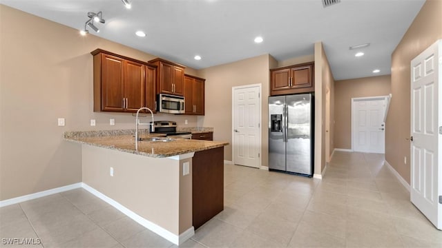 kitchen featuring recessed lighting, a sink, appliances with stainless steel finishes, light stone countertops, and brown cabinetry