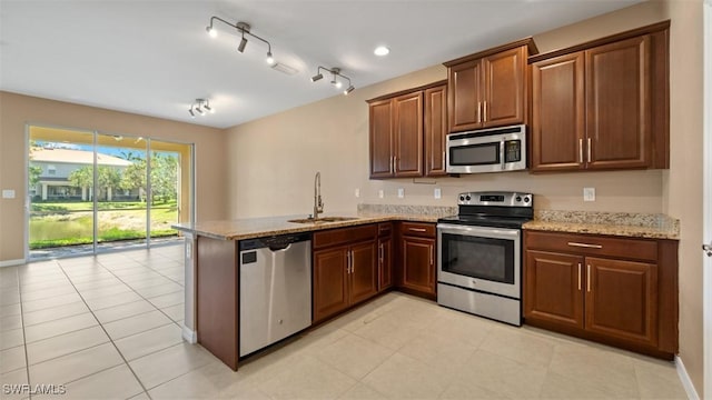 kitchen with appliances with stainless steel finishes, a sink, track lighting, light stone countertops, and a peninsula