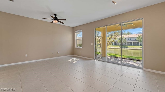 unfurnished room featuring a ceiling fan, a water view, baseboards, and light tile patterned floors