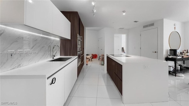 kitchen featuring white cabinets, a center island with sink, light countertops, and a sink