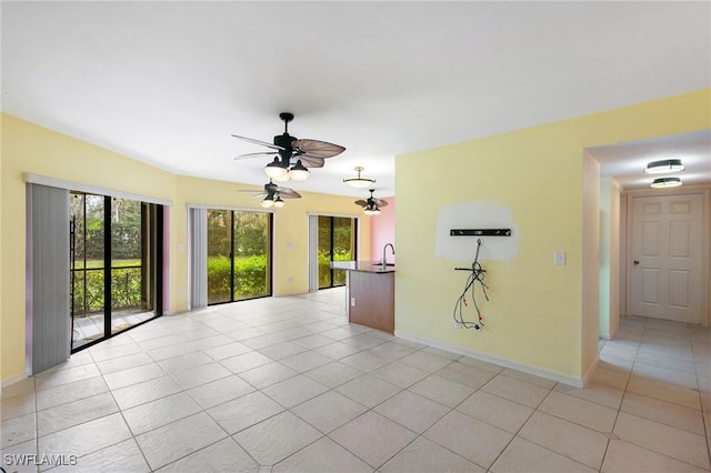 unfurnished room with light tile patterned floors, plenty of natural light, baseboards, and a sink