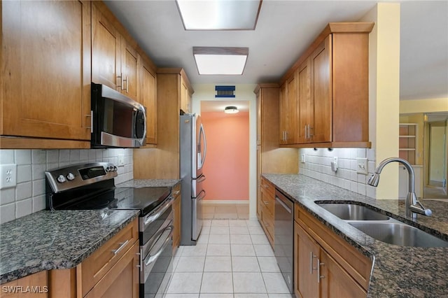 kitchen featuring brown cabinets, a sink, dark stone counters, appliances with stainless steel finishes, and light tile patterned floors