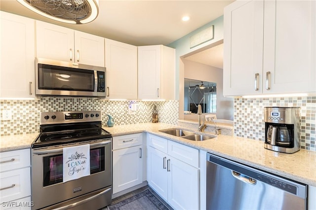 kitchen featuring decorative backsplash, light stone counters, stainless steel appliances, white cabinetry, and a sink