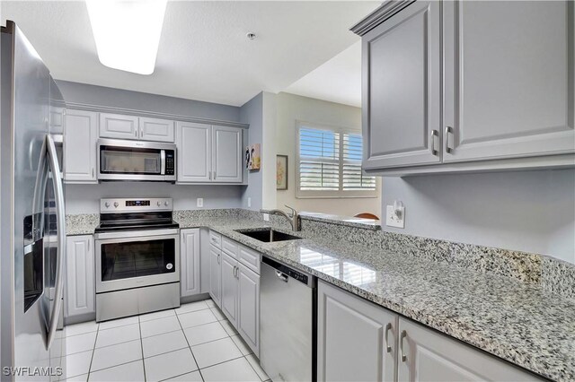 kitchen featuring light tile patterned floors, light stone countertops, stainless steel appliances, gray cabinetry, and a sink