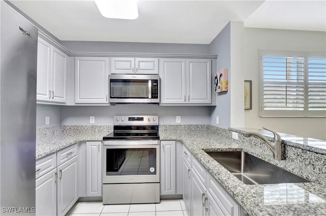 kitchen with light tile patterned floors, stainless steel appliances, a sink, and light stone countertops