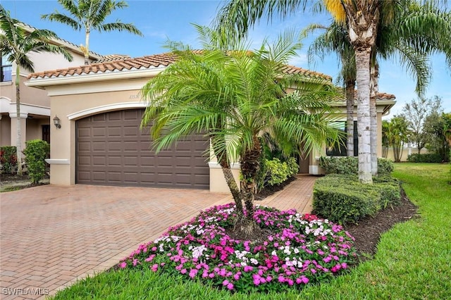 mediterranean / spanish home with a garage, decorative driveway, a tile roof, and stucco siding