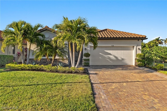 mediterranean / spanish house featuring decorative driveway, stucco siding, an attached garage, a tiled roof, and a front lawn