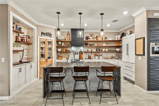 kitchen with open shelves, visible vents, a kitchen island with sink, white cabinetry, and a kitchen bar