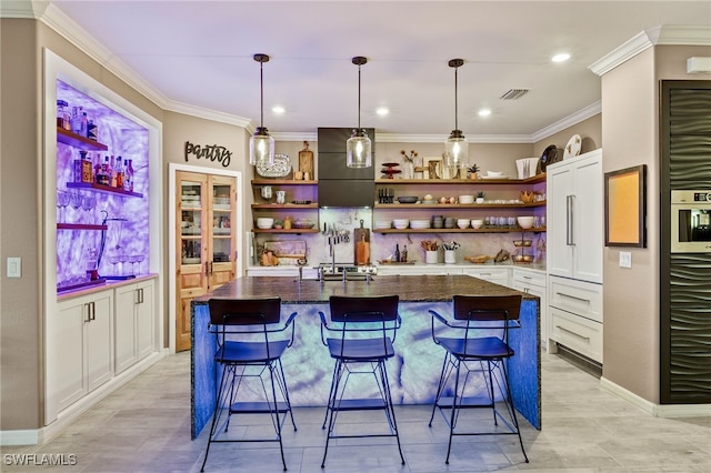 kitchen with open shelves, a breakfast bar, an island with sink, and white cabinetry