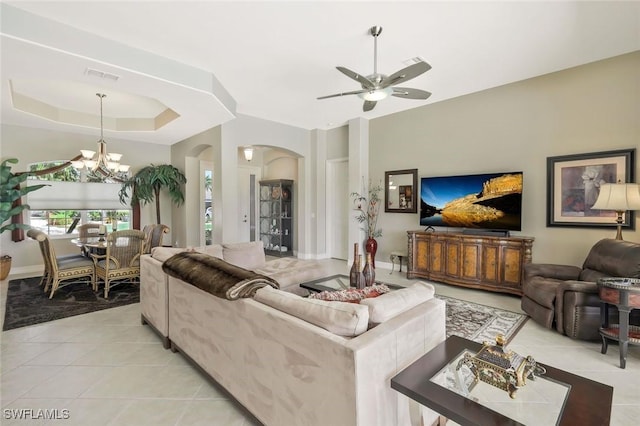 living area with light tile patterned floors, arched walkways, ceiling fan with notable chandelier, visible vents, and a tray ceiling