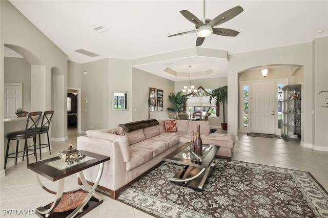 living room with arched walkways, light tile patterned flooring, ceiling fan with notable chandelier, baseboards, and a raised ceiling