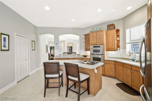 kitchen with arched walkways, stainless steel appliances, light countertops, a center island, and a kitchen bar