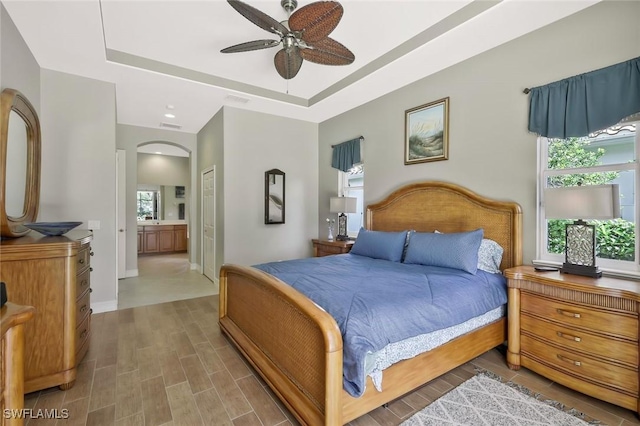 bedroom featuring ensuite bathroom, wood finished floors, baseboards, a closet, and a tray ceiling